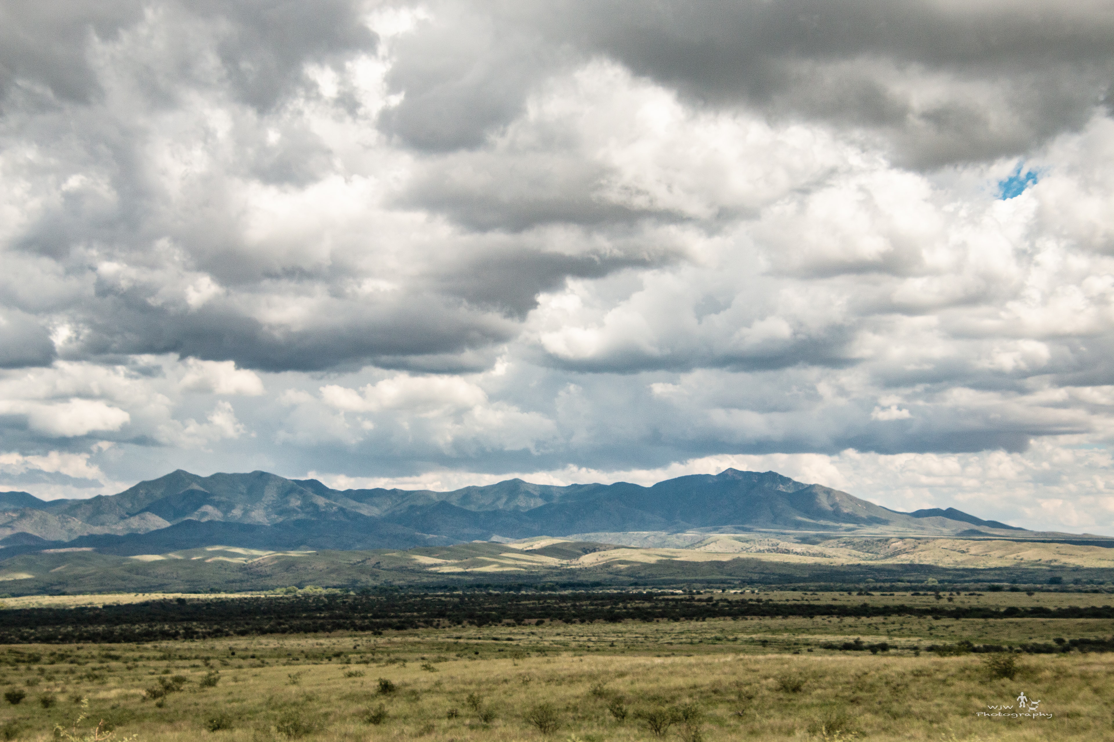 Sweeping Sky Islands grassland under dramatic storm clouds with mountain range in the distance