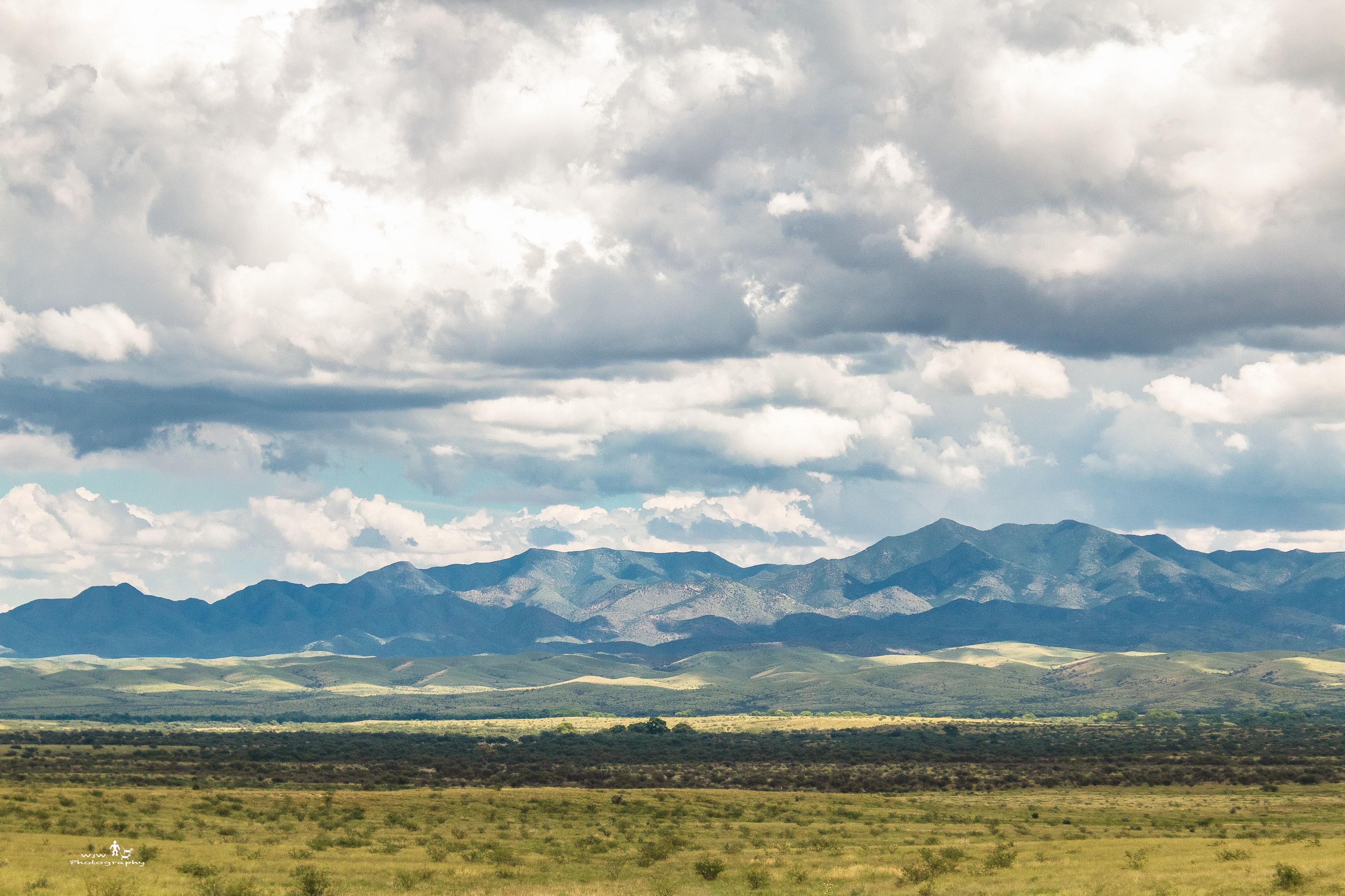 Rolling green hills with a dirt track winding toward the Santa Rita Mountains under a stormy sky