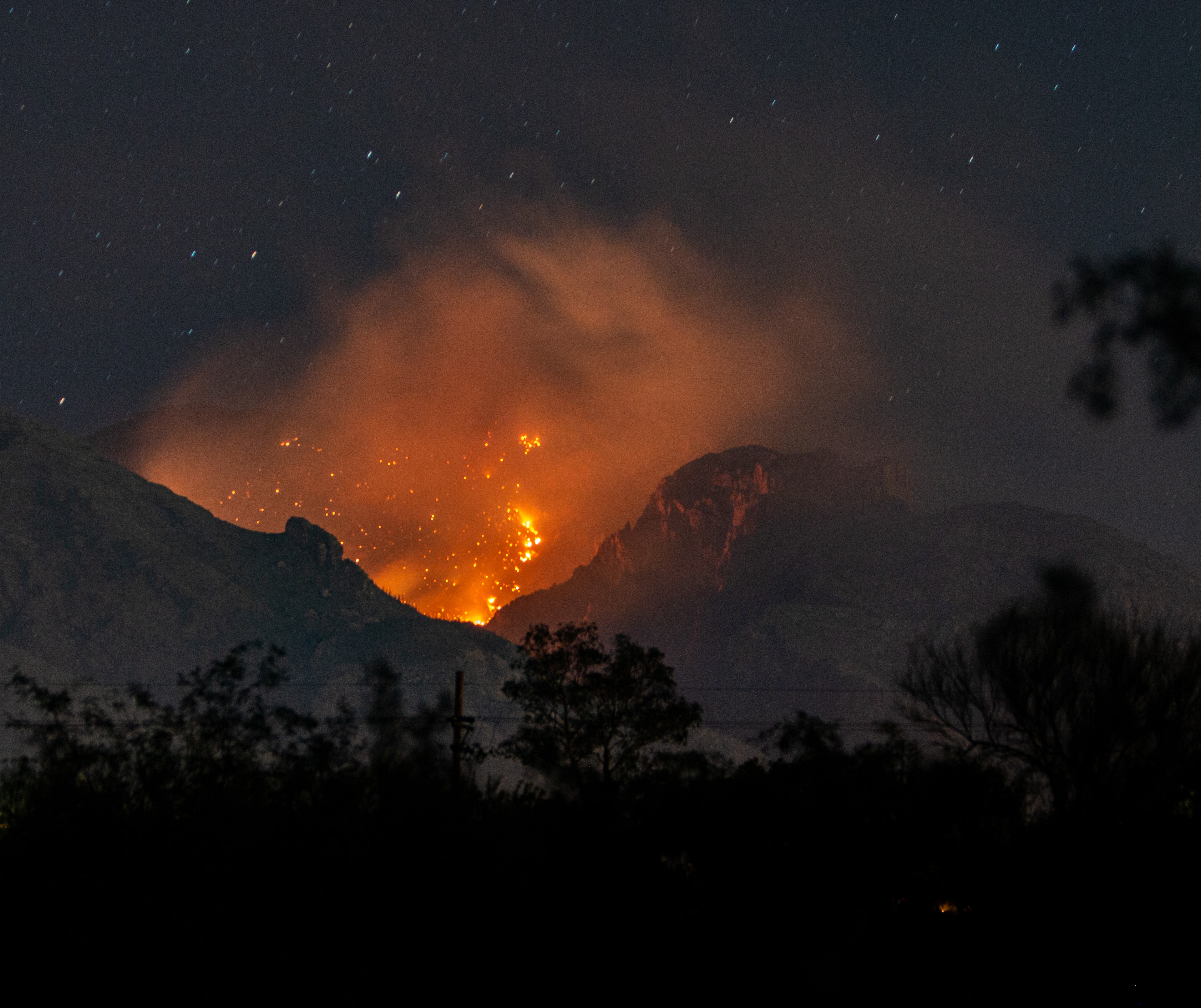 Bighorn Fire raging through the Catalina Mountains at night with orange flames and smoke billowing under a starry sky