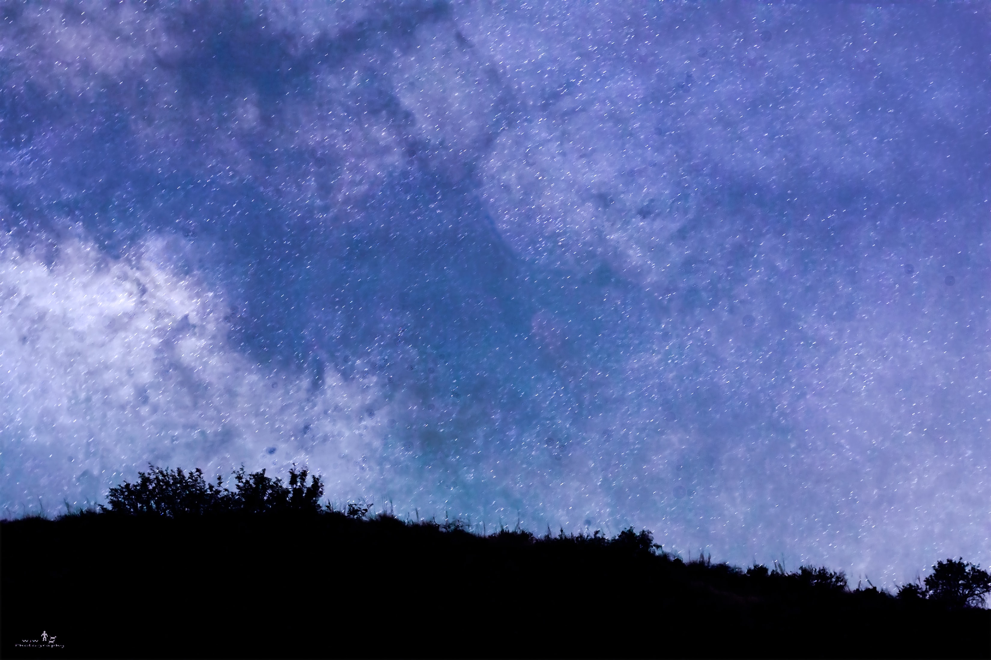 Milky Way galaxy arching over silhouetted treeline and hillside