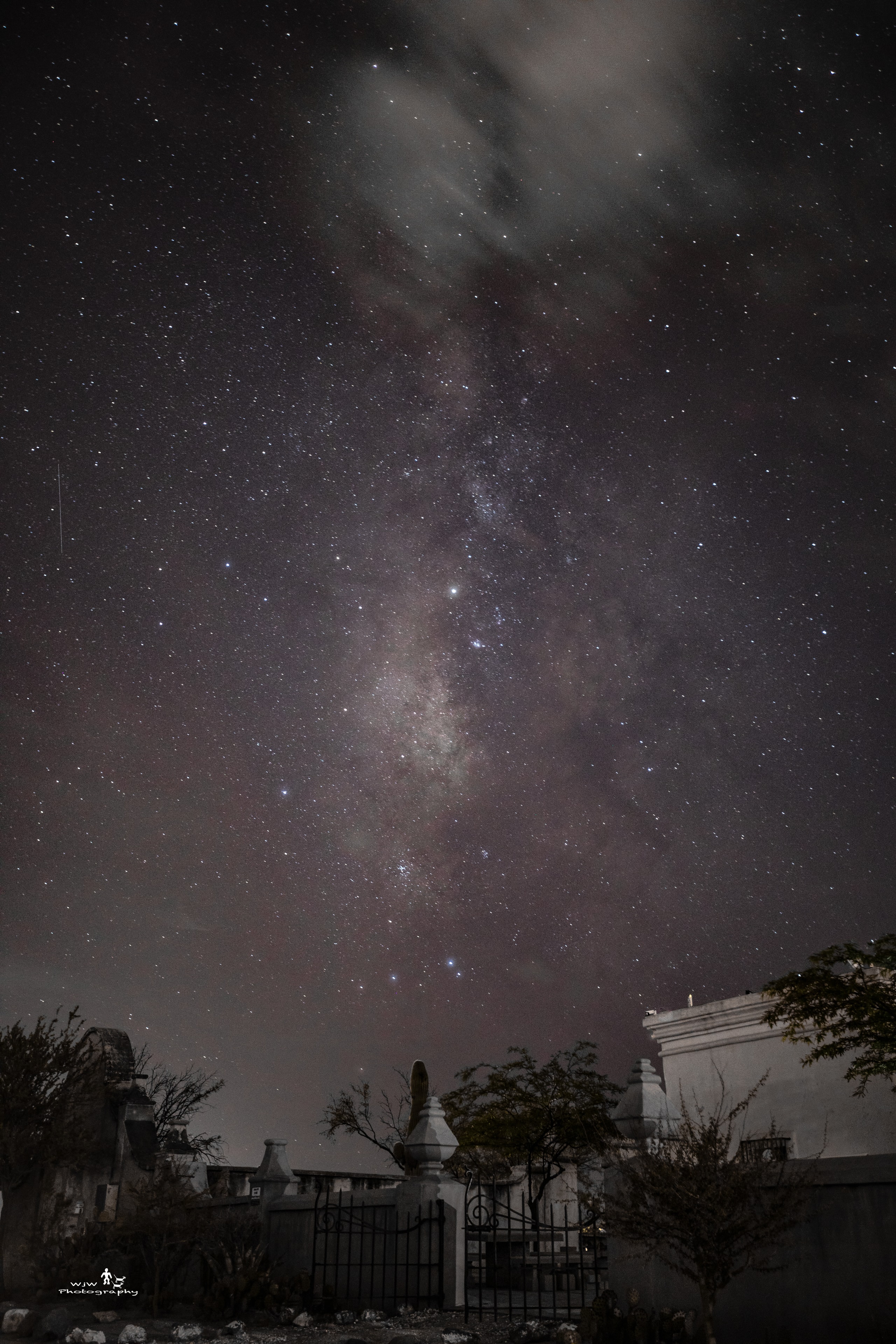 Milky Way rising above a historic building and iron gate at night with wispy clouds