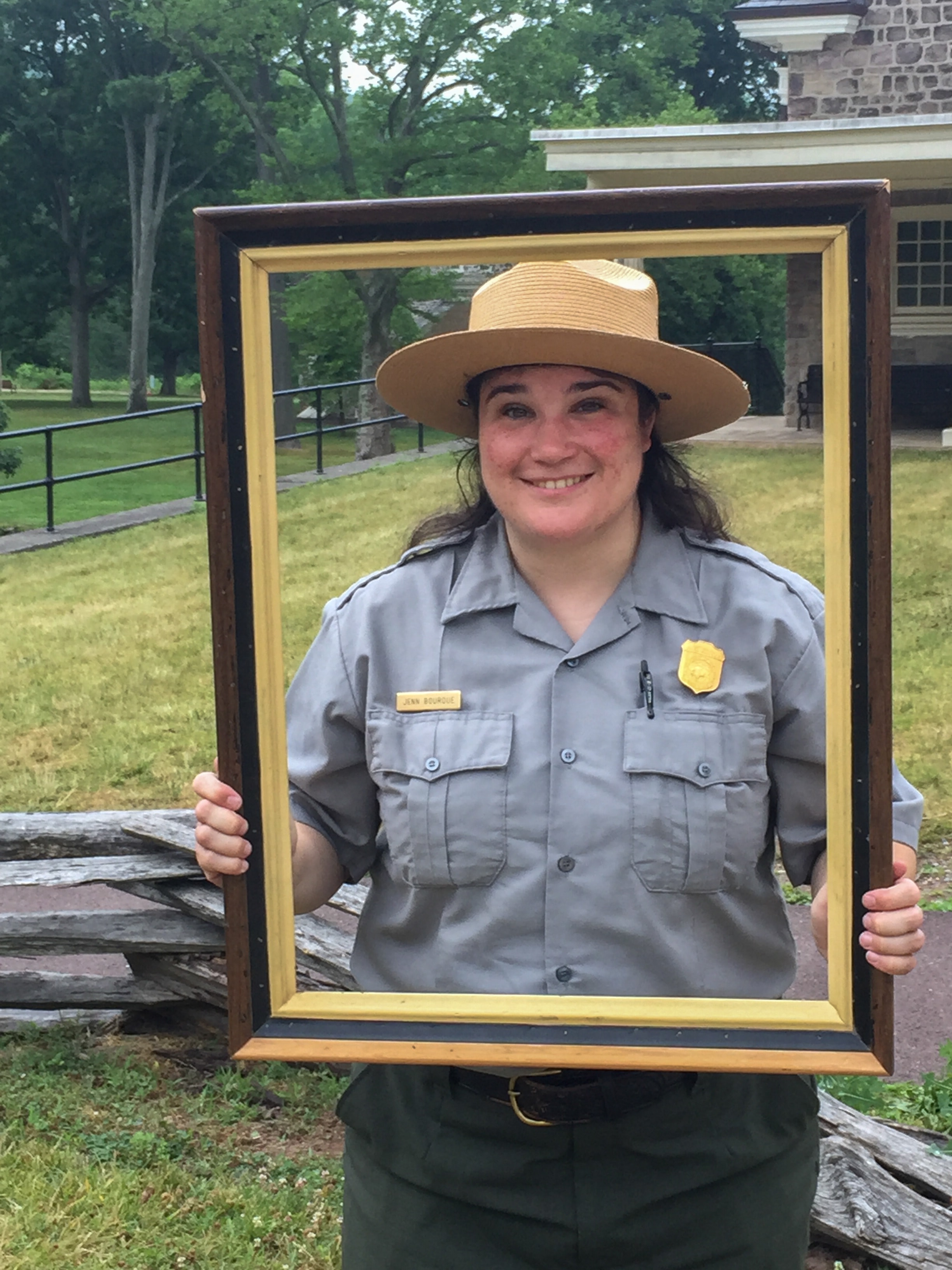 National Park Service ranger in uniform holding a picture frame outdoors at a historic site