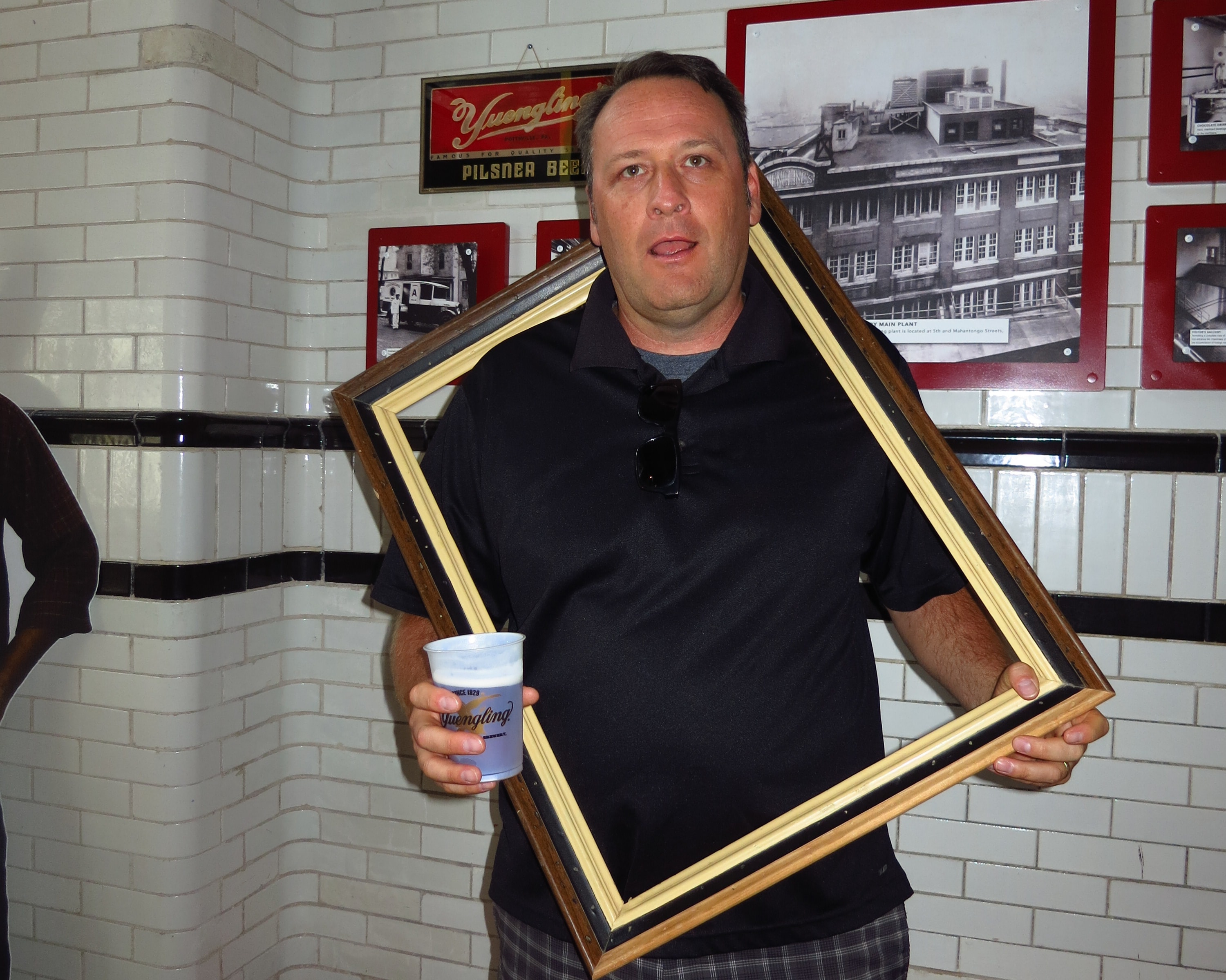 Man in a black polo holding a tilted picture frame and a cup of Yuengling ice cream inside the Yuengling brewery